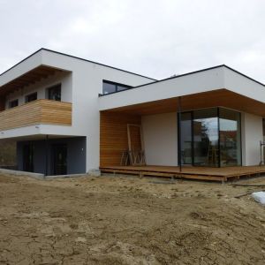 Flaches, modernes Haus mit weißer Fassade und großen Fensterflächen, Holzakzente im Eingangsbereich.