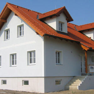 Zweigeschossiges Haus mit rotem Ziegeldach und weißer Fassade, Neubau.