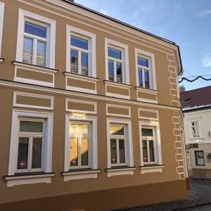 Zweigeschossiges Stadthaus mit beigefarbener Fassade und weißen Fensterrahmen, dekorative Stuckelemente an den Fensterumrahmungen