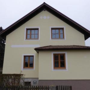 Wohnhaus mit heller Fassade und braunen Fensterrahmen, Dach mit dunklem Giebelvorsprung