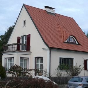 Weißes Einfamilienhaus mit rotem Satteldach, Balkon mit Schmiedeeisen-Geländer und Vorgarten