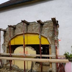 Alte Maueröffnung mit freigelegtem Ziegelbogen und abgeplatztem Putz an der Außenwand