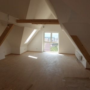 Dachgeschoss mit schrägen Decken, weiß gestrichenen Wänden und Holzbalken, saniert und leer