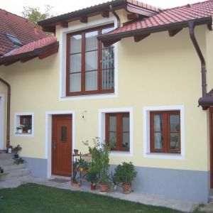 Gelbes Einfamilienhaus mit rotem Dach, brauner Eingangstür und Blumen im Vorgarten