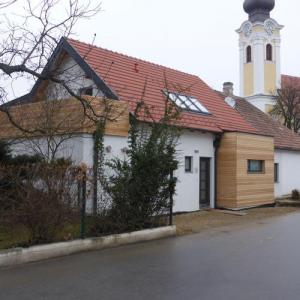 Kleines Haus mit rotem Dach, weißer Fassade und einer Kapelle im Hintergrund