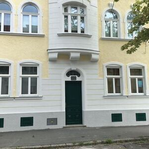 Dreigeschossiger Altbau mit gelber Fassade, weißen Fensterrahmen und grünem Eingangsportal