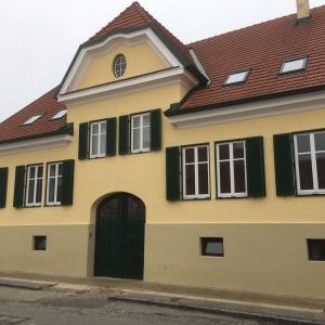 Altbau mit gelber Fassade, roten Dachziegeln, grünen Fensterläden und Rundbogen-Hauseingang