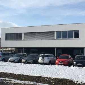 Zweigeschossiges Bürogebäude mit großflächiger Fensterfront, davor geparkte Autos auf schneebedecktem Boden