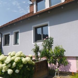 Haus mit weißer und rosafarbener Fassade, dunklen Fensterrahmen und blühenden Hortensien im Vorgarten