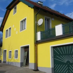Helles gelbes Haus mit grünem Garagentor, überdachtem Balkon und Satteldach