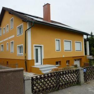 Ockergelbes Wohnhaus mit weißen Fensterrahmen und flachem Eingangspodest