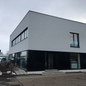 Modernes zweigeschossiges Gebäude mit flachem Dach, weißer Putzfassade und dunkler Fensterfront im Erdgeschoss
