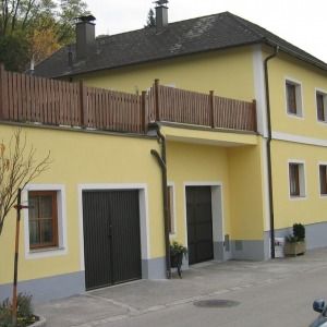 Zweifamilienhaus mit heller Fassade, braunem Balkon und flachem Garagenanbau