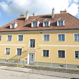 Mehrfamilienhaus mit gelber Fassade und großem Dachgeschossbereich, mehrere Eingänge und Fensterachsen