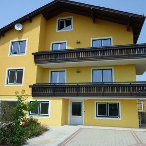 Dreigeschossiges Wohngebäude mit gelber Fassade, dunklem Balkon und mehreren Wohnungen