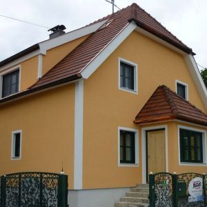 Kleines Wohnhaus mit ockergelber Fassade, rotem Dach und überdachtem Eingangsbereich