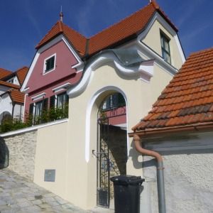 Historisches Gebäude mit geschwungener Fassade, rotem Dach und verzierter Mauer, restauriert und farblich akzentuiert