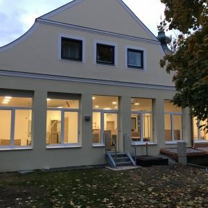 Großes Gebäude mit heller Fassade und zahlreichen Fenstern, modernes Satteldach und gepflegter Gartenbereich mit Laub