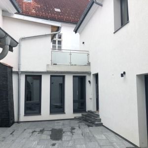 Innenhof eines sanierten Hauses mit weißer Fassade, großem Glaselement und kleinem Balkon