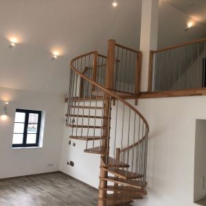 Heller Raum mit weißer Wand, dunklem Holzboden und Holz-Wendeltreppe, die zu einer Galerie führt