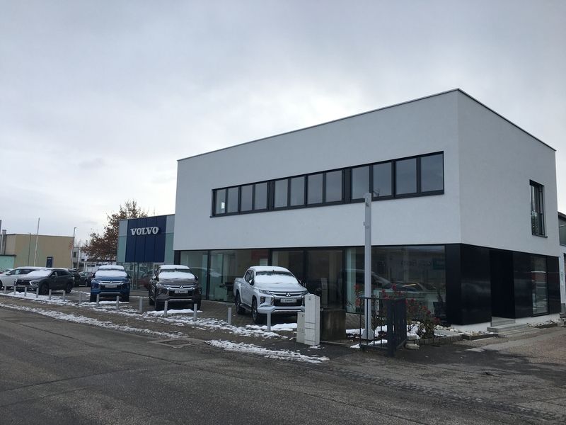 Modernes Autohaus mit zweigeschossigem, rechteckigem Gebäude in weißer und schwarzer Farbgebung. Große Fensterfronten im Erdgeschoss, schmale Fensterreihe im Obergeschoss.