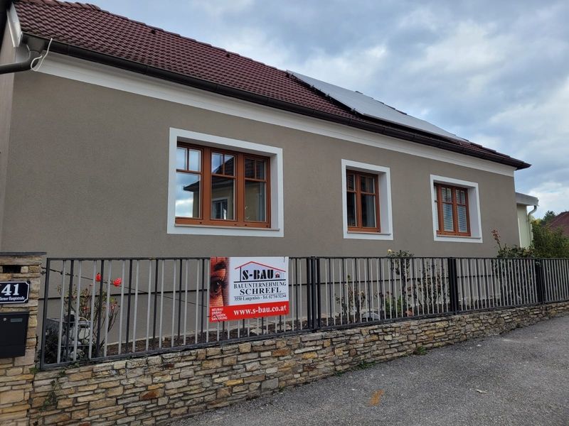 Moderne Küche mit schwarzer Arbeitsplatte, Spüle und Kochfeld, beleuchtet von Tageslicht durch ein großes Fenster