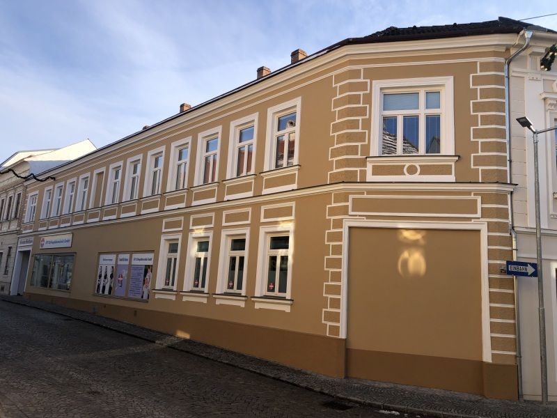 Zweigeschossiges Stadthaus mit hellbrauner Fassade und weißen Stuckelementen. Die Fenster im Erdgeschoss und Obergeschoss sind gleichmäßig angeordnet und mit Zierleisten umrahmt.